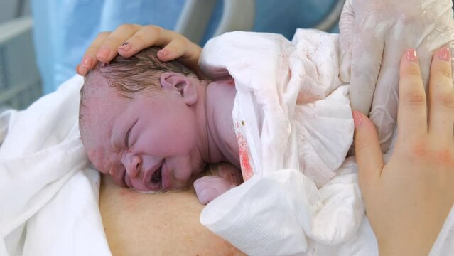 Young mother holding newborn child after labor. Emotional moment of child birth in maternity hospital
