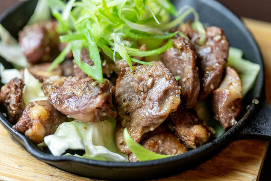 スキレットで香ばしく焼き上げられた鶏のハツと砂肝のガーリック炒め、たっぷりの刻みねぎを添えたスタミナ居酒屋メニュー | Sizzling Garlic Sauteed Chicken Hearts and Gizzards in a Skillet, Topped with Fresh Green Onions