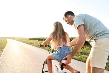 Back view of father teaching his little daughter how to ride a bike