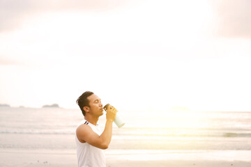 asian sport man drinking water while enjoying a morning run on the beach