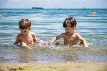 Happy family playing in blue water of swimming pool on a tropical resort at the sea. Summer vacations concept. Two brother kids are best friends