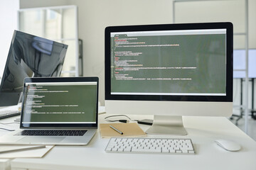 Horizontal image of workplace of programmer with computer and laptop with software on the screen