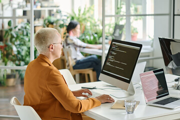 Rear view of female developer with short hair sitting at her workplace with computer monitor and...