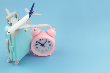 Time for travel and vacation concept. Airplane model with suitcase and clock on blue background....