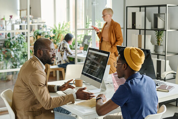 African programmers discussing software together while sitting at table with computer during meeting