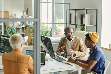 Colleagues sitting at table with computers during meeting and discussing new project in team