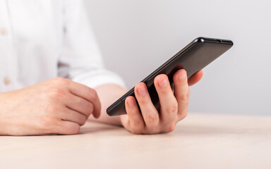 Woman hand closeup holding smartphone. Female sitting at table and reading electronic book or news article, checking social media or running Internet. High quality photo