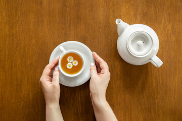A cup of chamomile tea and a teapot on a wooden background.