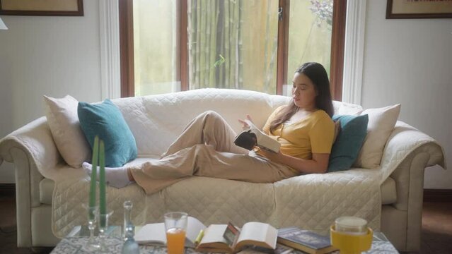 Female Relaxing At Home While Reading Books Inside The Living Room. Medium Shot