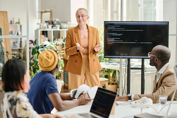 Mature businesswoman presenting report of new computer software to her colleagues at meeting at office
