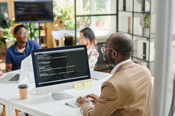 Rear view of African programmer writing code on computer sitting at his workplace at office