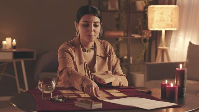 Waist up POV with slowmo of young fortune teller looking at camera while laying out tarot cards on table and predicting future