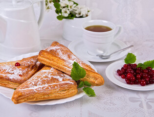 sweet pastries with red currant berries, with mint leaves, on a white dish, a cup of tea on a white background