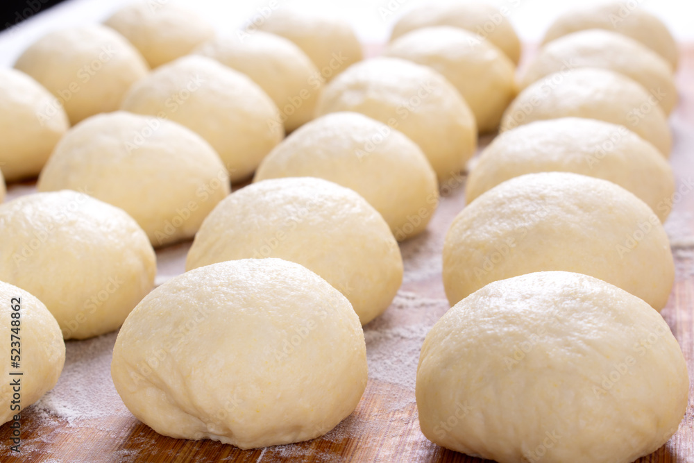 Wall mural Yeast dough balls on the wooden board with flour. Preparing to bake buns, pizza or bread