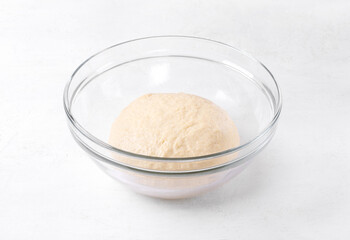 Fototapeta na wymiar Yeast dough in glass bowl on white table. Proofing baking technique