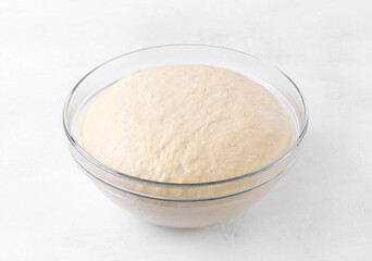 Yeast dough rising in glass bowl on white table. Proofing baking technique