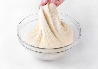 Kneading yeast dough in glass bowl on white table