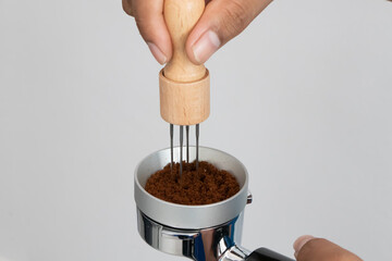 Hand using a coffee distributor tool to evenly level ground coffee in a portafilter for perfect...