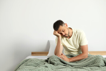 Sleep deprived man sitting on bed at home. Space for text