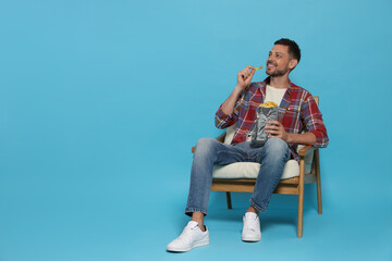 Handsome man eating potato chips on light blue background, space for text