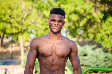 Portrait of a young fit shirtless black man smiling looking at camera in a park outdoors. Fitness and sport lifestyle.
