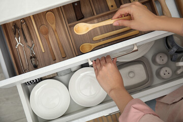 Woman taking wooden spoon from drawer of kitchen cabinet, top view - obrazy, fototapety, plakaty