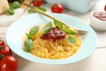 Tasty spaghetti squash with tomato sauce, cheese and basil served on white wooden table, closeup