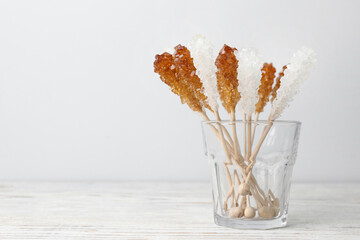 Sticks with sugar crystals in glass on white wooden table, space for text. Tasty rock candies