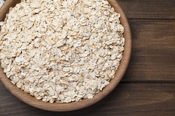 Raw oatmeal in bowl on wooden table, top view