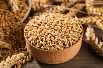 Fototapeta na wymiar Wheat grains with spikelets on wooden table, closeup