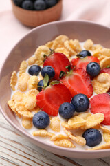 Bowl of tasty crispy corn flakes with milk and berries on white wooden table, closeup