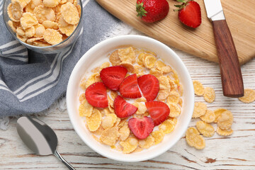 Bowl of tasty crispy corn flakes with milk and strawberries on white wooden table, flat lay