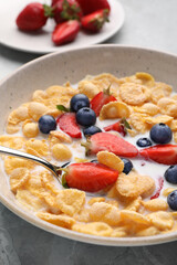 Bowl of tasty crispy corn flakes with milk and berries on light grey table, closeup