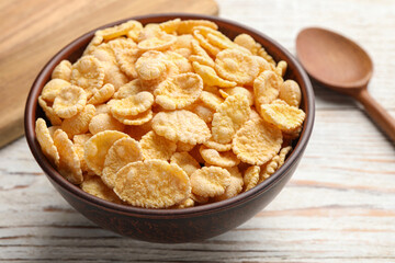 Bowl of tasty corn flakes and spoon on white wooden table, closeup