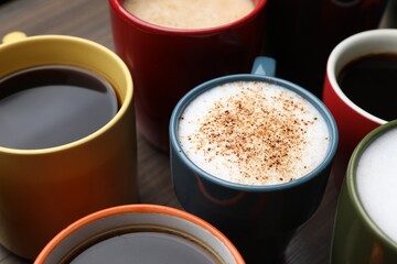 Many different cups with aromatic hot coffee on wooden table, closeup