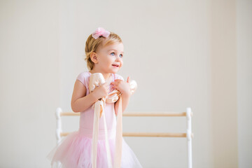 Portrait of a cute blue-eyed baby ballerina in pink hugging pointe shoes.