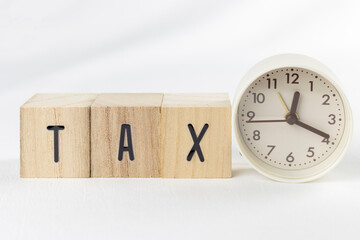 木のブロックのTAXと、アナログ時計。税金の支払い期限イメージ