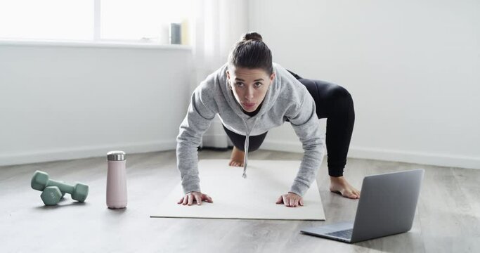 Fitness, exercise and healthy woman training at home doing spiderman pushups in her workout routine on a mat to get a stronger upper body. Young female athlete exercising to active tutorial videos