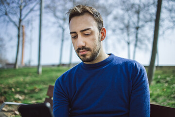 Close-up of young man looking at and typing on cell phone sitting in a park on a sunny day