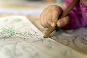 Child drawing random lines on paper, selective focus.