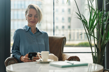 Professional Business woman using phone sitting in cafe. Successful inspired entrepreneur female having a coffee while texting on smartphone app