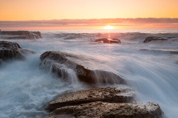 Silky waves splash over sharp rocks at sunrise