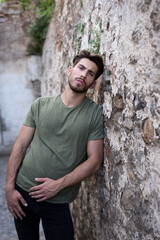 Confident bearded man leaning on weathered wall and looking at camera