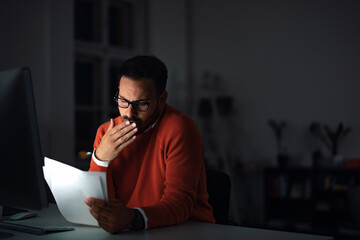 Focused man reading some notes, checking them, working overtime.