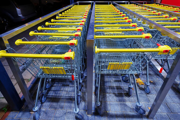 Row of stacked metal shopping carts with yellow handles near of supermarket