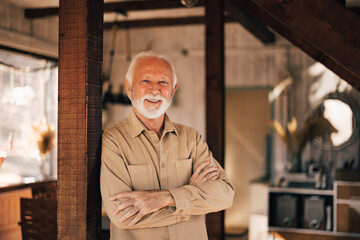 Portrait of an mature man, smiling for the camera, hands crossed, leaning on the wooden post.