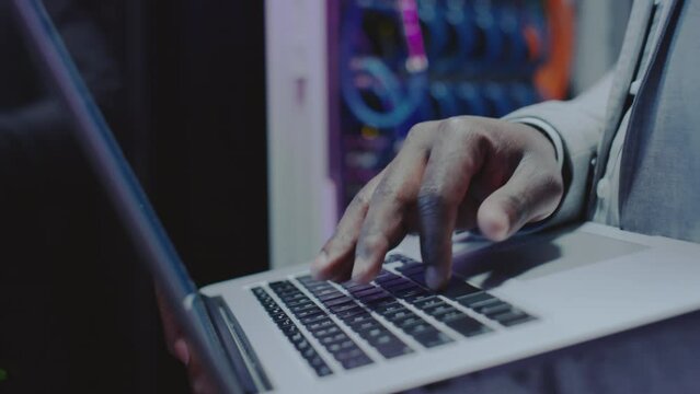 Tilt up close up shot of African American data center worker using laptop in server room