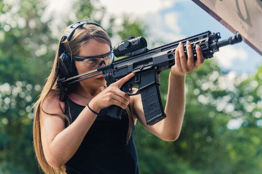 Young caucasian woman wearing protective goggles and headphones practising with submachine gun on outdoor shooting range. Horizontal shot. High quality photo