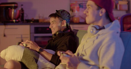 Expression of emotions on the face of video game players. Two guys use controllers in their hands. Move bodies, experience emotions. Evening room.