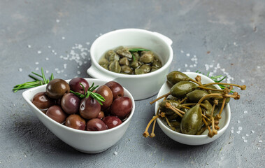 Caper berries and olives on white plate with fresh basil leaves on a gray background. Mediterranean snack assortment. banner, menu, recipe place for text, top view